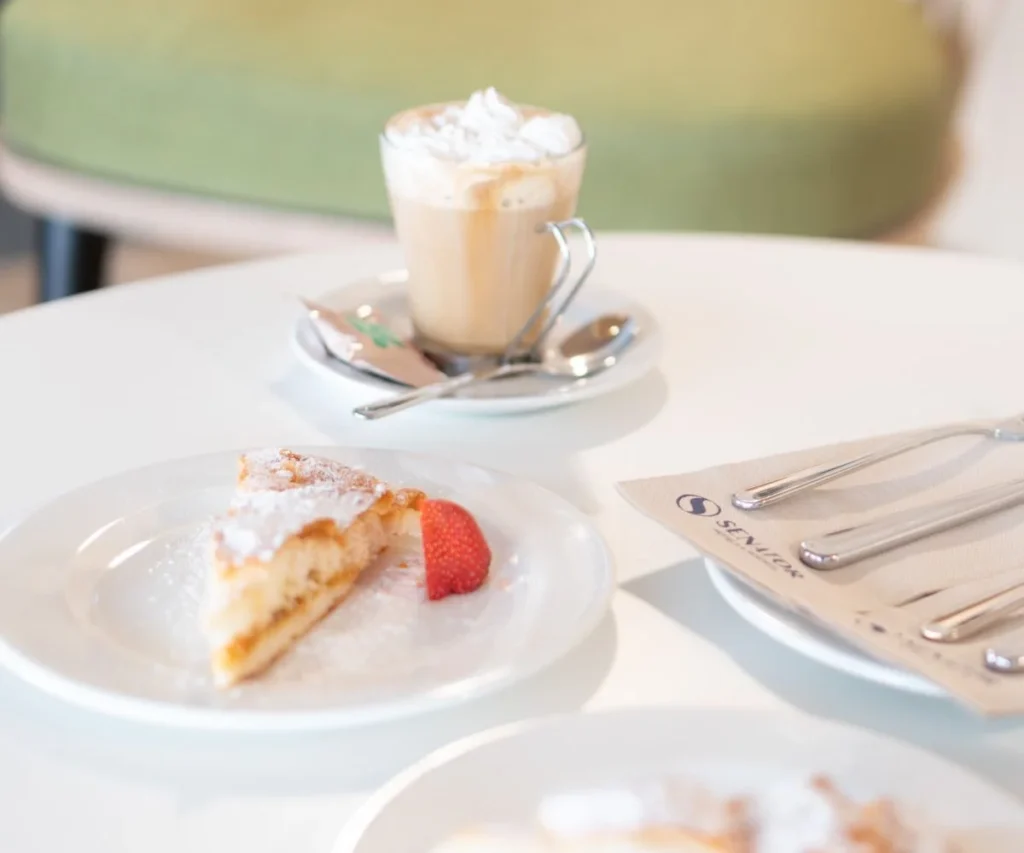 Tarta con crema y fresas en plato, con caf&eacute; con leche y plato de cubiertos