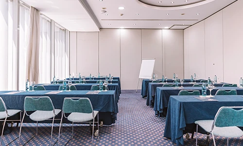 Sala de conferencias vac&iacute;a con mesas, sillas y un rotafolios al fondo.