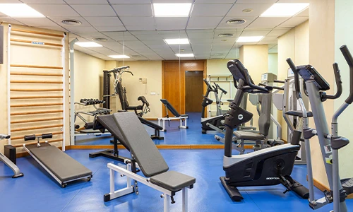 Gimnasio con m&aacute;quinas de ejercicio y un espejo grande en la pared.