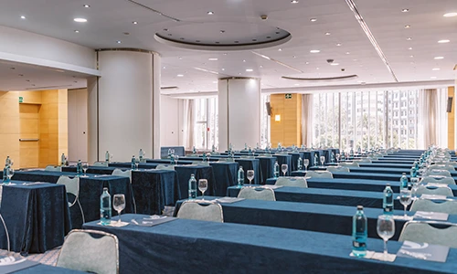 Sala de conferencias con mesas y sillas alineadas y botellas de agua.