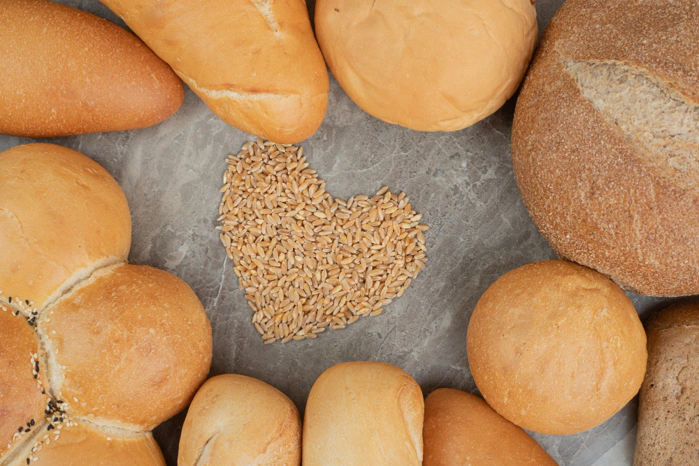 Diferentes hogazas y tipos de pan sin gluten con un pu&ntilde;ado de trigo haciendo un coraz&oacute;n en el medio - Hoteles sin gluten SHR