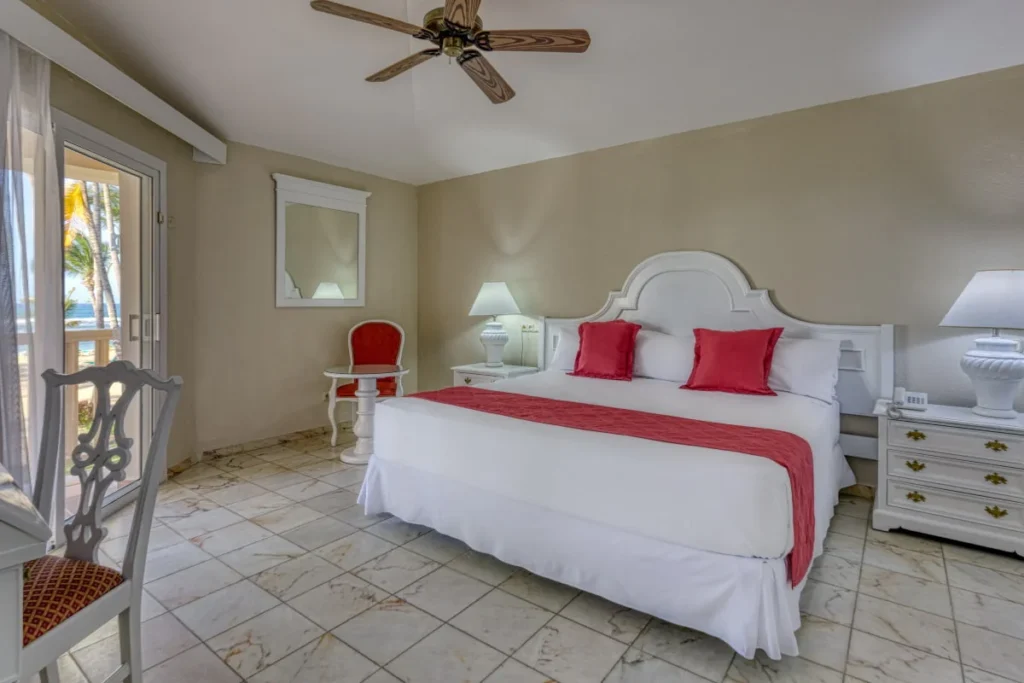 Dormitorio con cama doble blanca y s&aacute;banas rojas, l&aacute;mparas y ventilador de techo