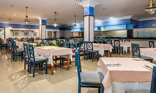 Restaurante amplio con mesas cubiertas de mantel y sillas azules.