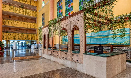 Recepci&oacute;n de hotel con vitrales, plantas y decoraci&oacute;n colorida.