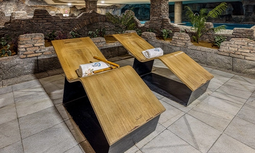 Dos tumbonas de madera junto a una piscina en un ambiente r&uacute;stico.