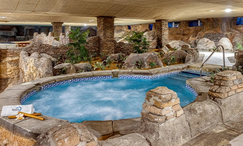 Jacuzzi interior con paredes de piedra y jard&iacute;n decorativo.