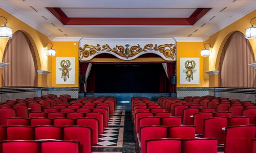 Peque&ntilde;o teatro con asientos rojos y escenario decorado.