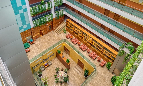 Vista de un atrio interior con plantas, muebles y balcones en varios niveles.