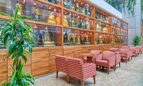 Sala con estantes de relojes antiguos y sillas rayadas frente a mesas peque&ntilde;as.