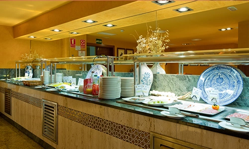 Buffet con platos, bandejas de comida y decoraci&oacute;n en un restaurante iluminado.