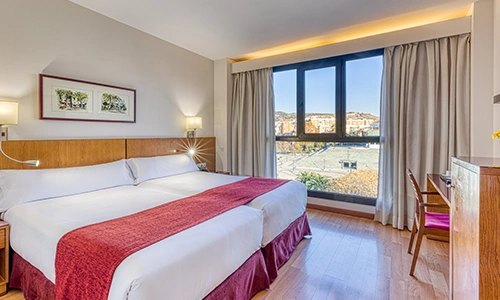 Habitaci&oacute;n de hotel con cama doble, ventanas grandes y decoraci&oacute;n moderna.