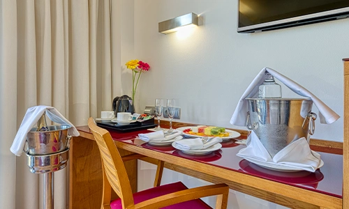 Mesa con vajilla, cubetas de hielo, flores y una televisi&oacute;n montada en la pared.