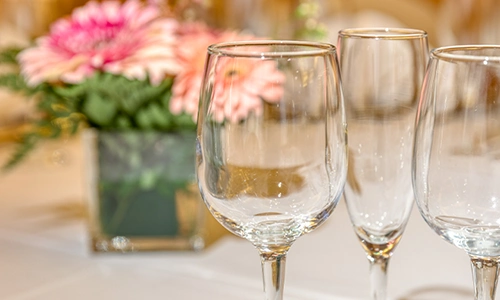 Copas de cristal sobre una mesa con flores difuminadas al fondo.