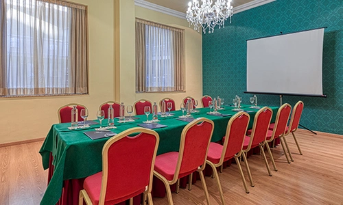 Sala de reuniones con mesa rectangular, sillas rojas y proyector.