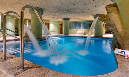 Piscina interior climatizada con cascadas y escaleras de metal.