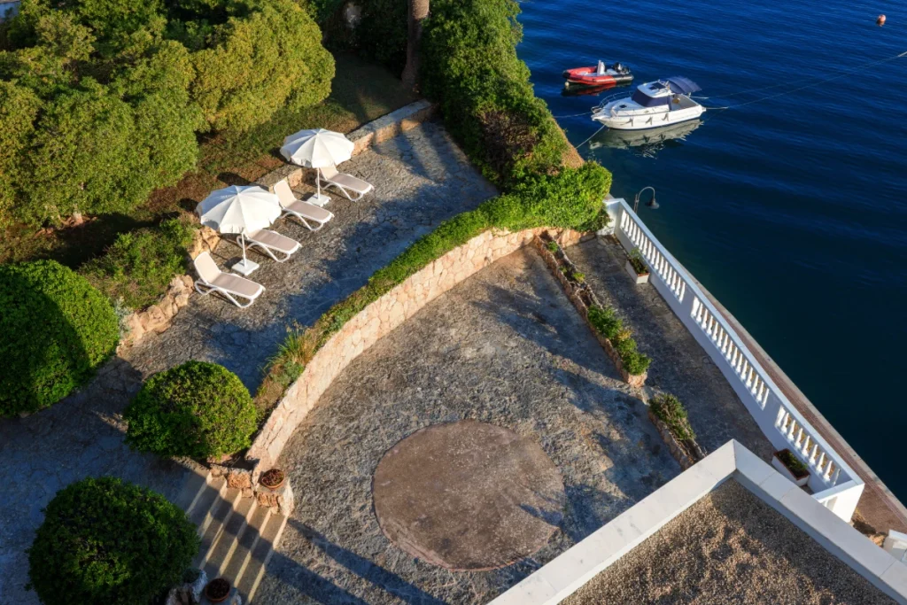 Vista a&eacute;rea de embarcaderos, barcos y tumbonas junto al mar, con piscina y jard&iacute;n