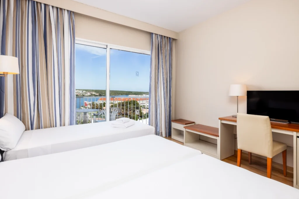 Habitaci&oacute;n de hotel con cama doble, escritorio y ventana con vista al mar.