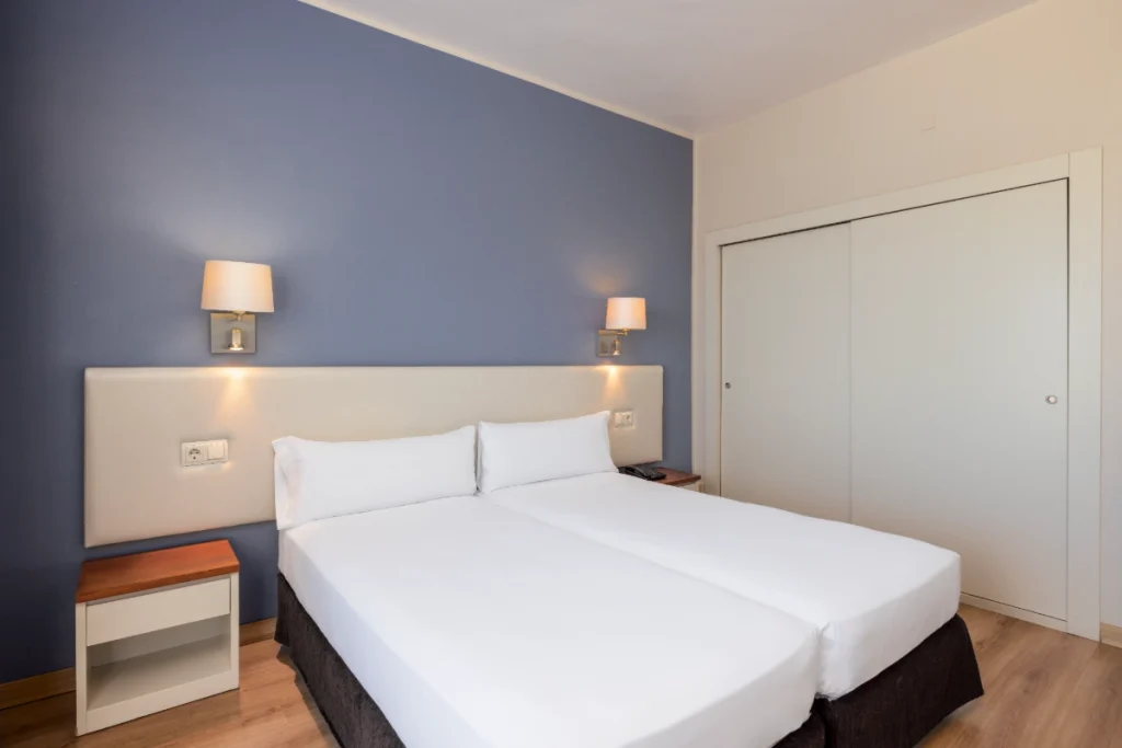 Dormitorio moderno con cama blanca, l&aacute;mparas y pared azul.