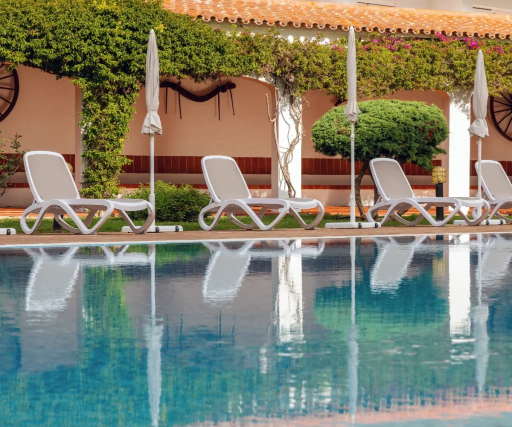 Piscina con cuatro tumbonas blancas y jard&iacute;n verde, bajo p&eacute;rgola con cortinas