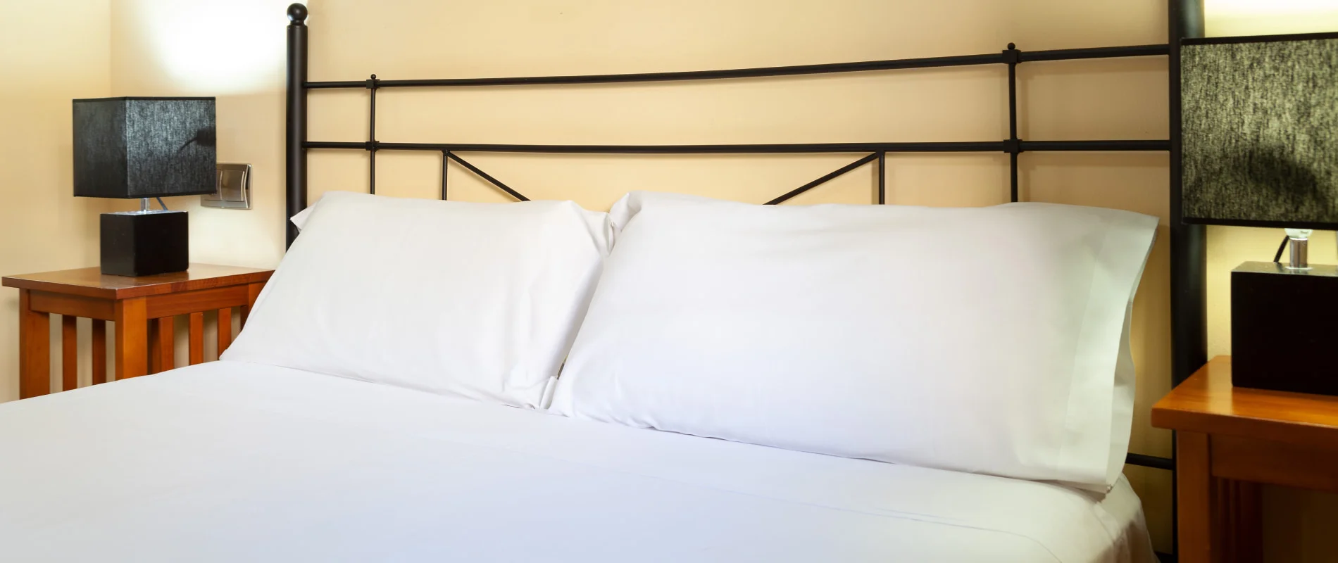 Cama doble con s&aacute;banas blancas en habitaci&oacute;n de hotel, vista frontal