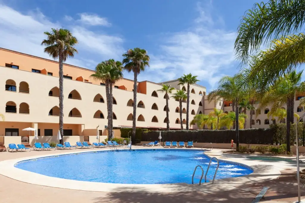 Piscina azul con palmeras y edificio hotelero bajo cielo despejado