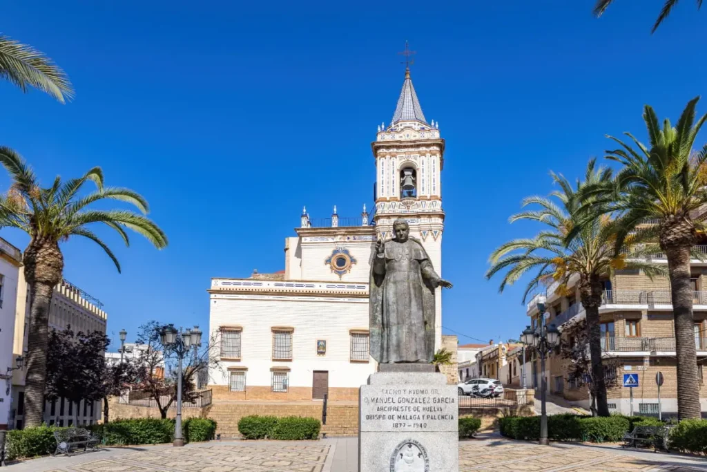 Iglesia y estatua de bronce con palmeras bajo cielo azul.