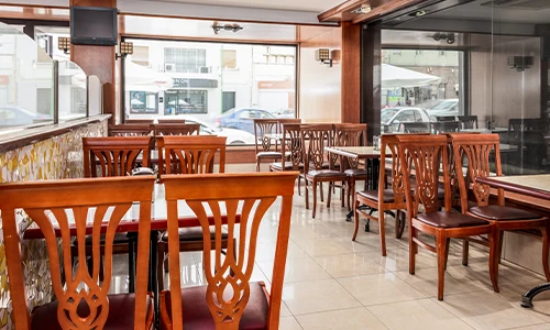 Restaurante con sillas de madera y mesas, ambiente tranquilo y vac&iacute;o.