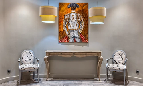 Sala con consola, dos sillas, arte de torero y l&aacute;mparas colgantes.