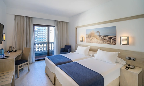 Habitaci&oacute;n de hotel con dos camas, balc&oacute;n y decoraci&oacute;n moderna.