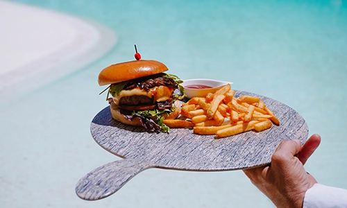 Hamburguesa y papas fritas servidas en un plato frente a una piscina.