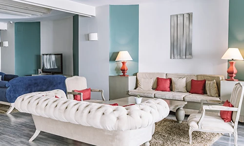 Sala moderna con sof&aacute;s claros, cojines rojos y l&aacute;mparas de mesa.