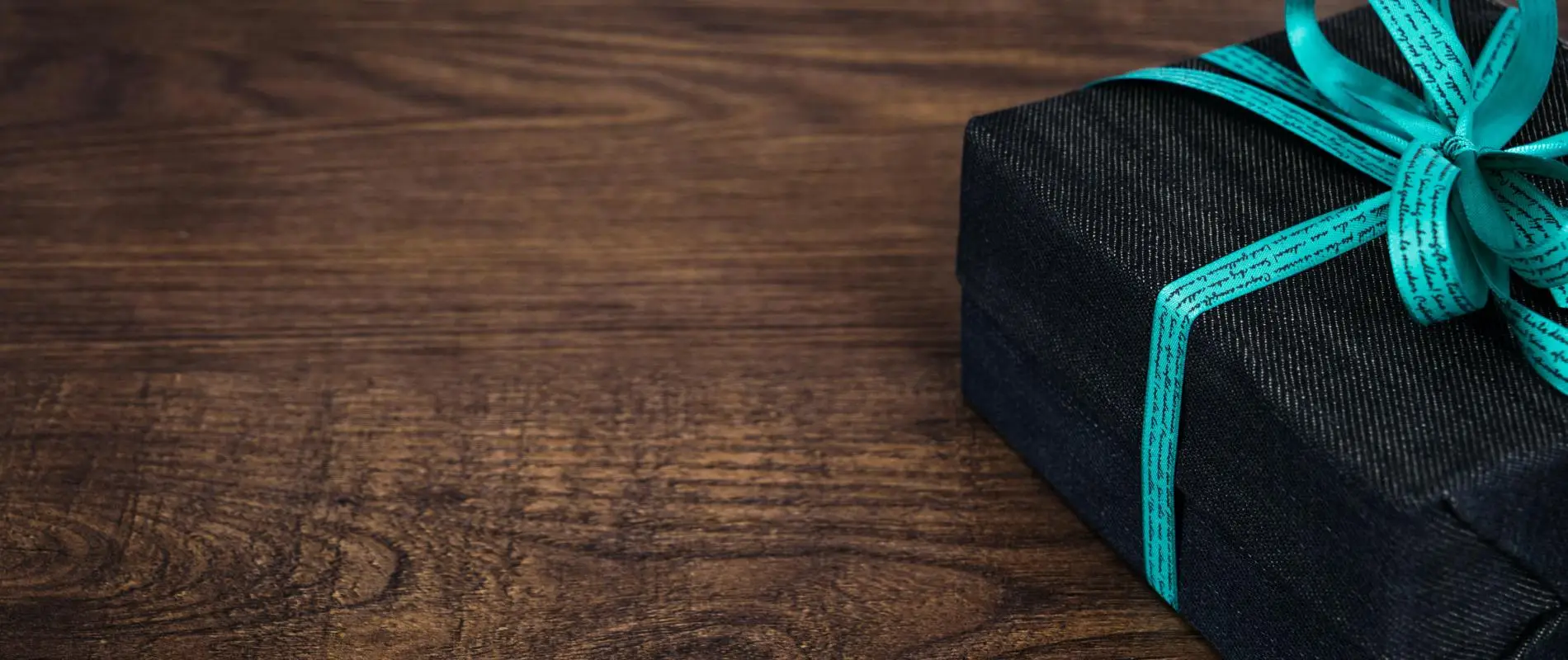 Caja de regalo negra con mo&ntilde;o verde sobre madera, sin texto