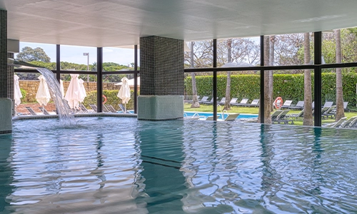 Piscina interior con cascada, vista al jard&iacute;n y tumbonas al aire libre.