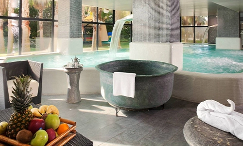 Spa con piscina interior, jacuzzi y frutas frescas en una bandeja de madera.