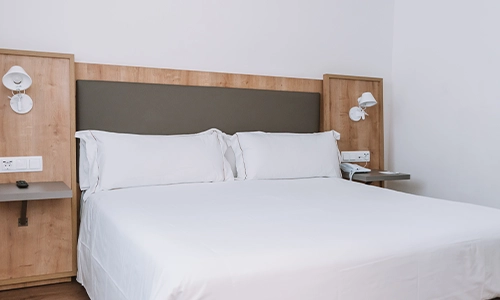 Cama de matrimonio con ropa de cama blanca en habitaci&oacute;n moderna y simple.