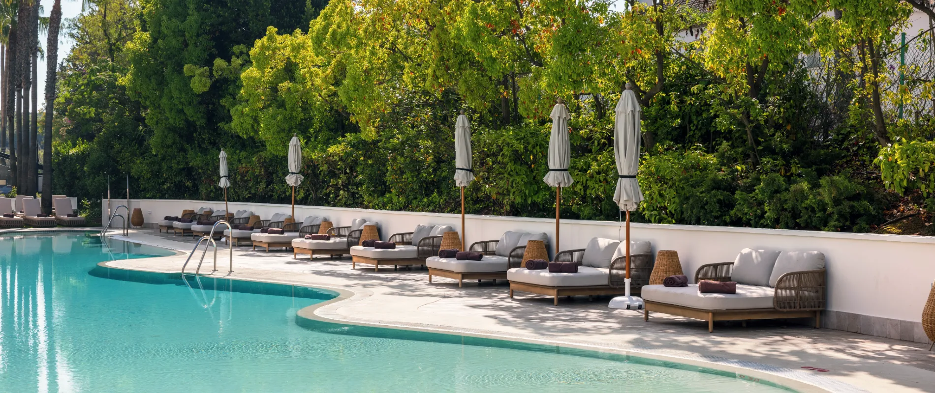 Piscina con tumbonas y sombrillas junto a un jard&iacute;n verde exuberante