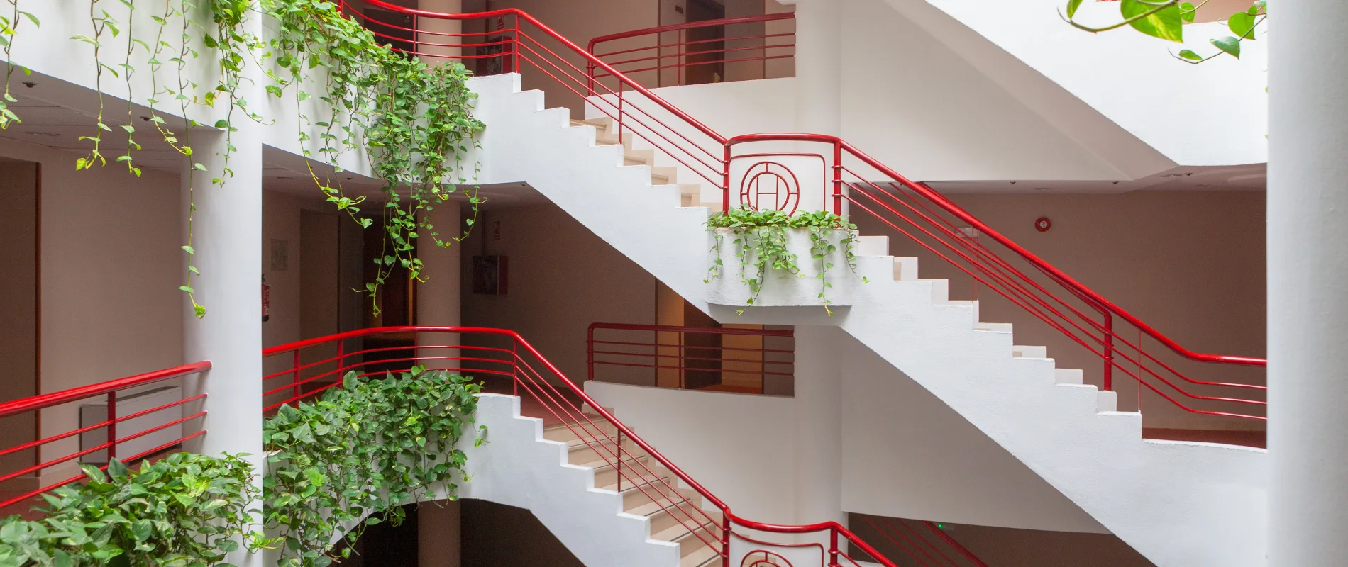 Escalera interior blanca con barandales rojos y plantas colgantes verdes