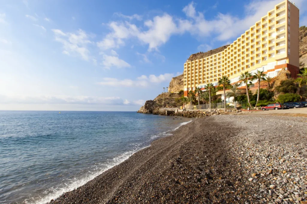 Hotel junto al mar en la costa rocosa, con palmeras y cielo despejado