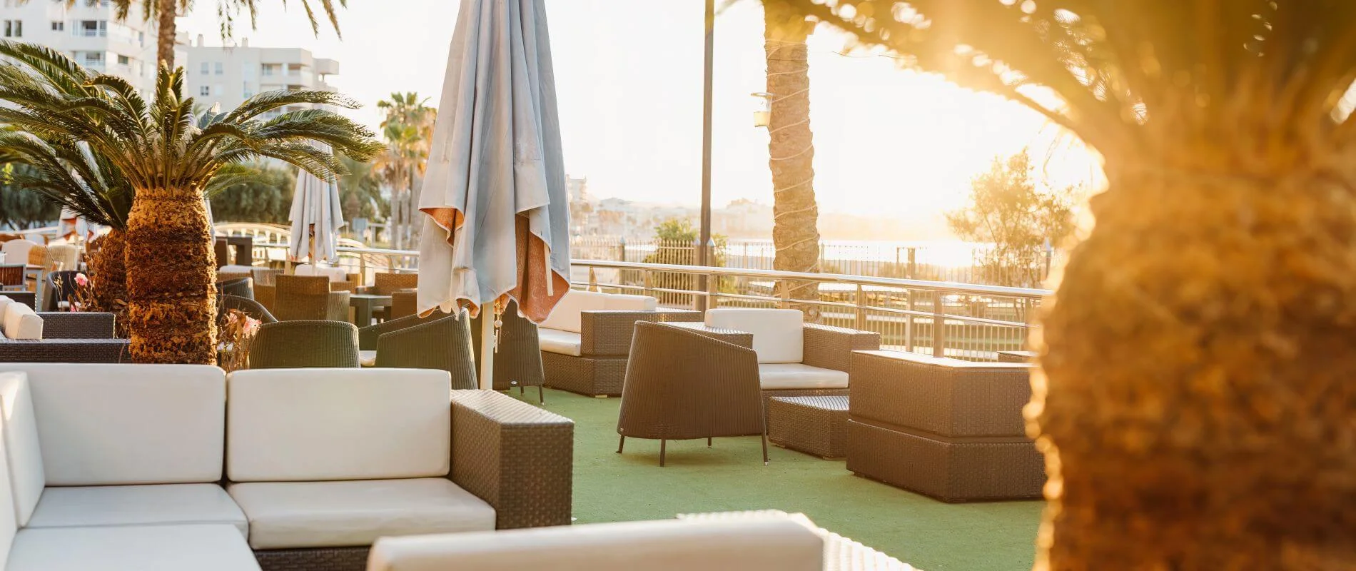 Terraza con sillones de exterior, sombrilla y palmeras al atardecer.
