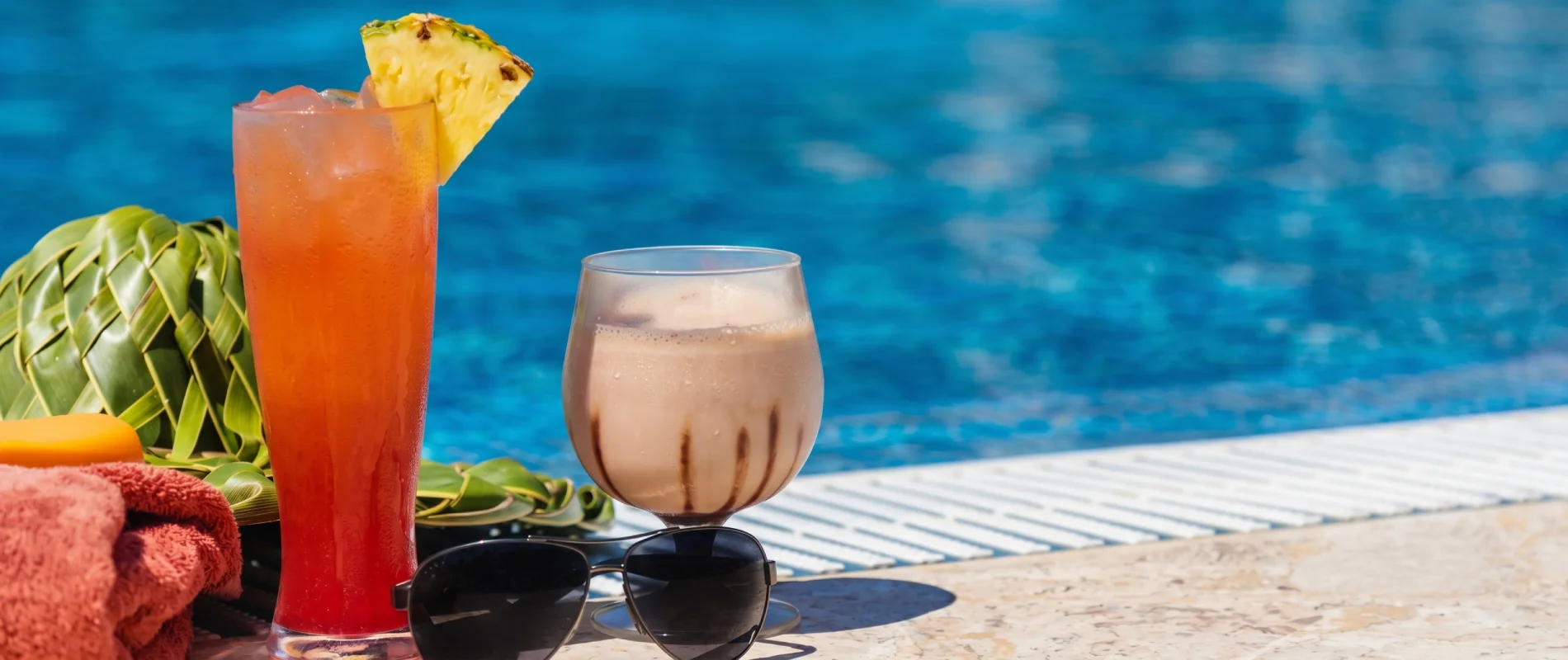 C&oacute;ctel tropical en vaso alto, pi&ntilde;a y pajilla junto a la piscina azul
