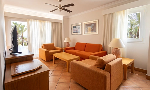 Sala de estar con sof&aacute;, sillones y mesa de madera, ventilador y TV.