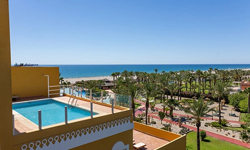 Piscina en la terraza con vista al mar y palmeras en un d&iacute;a soleado.