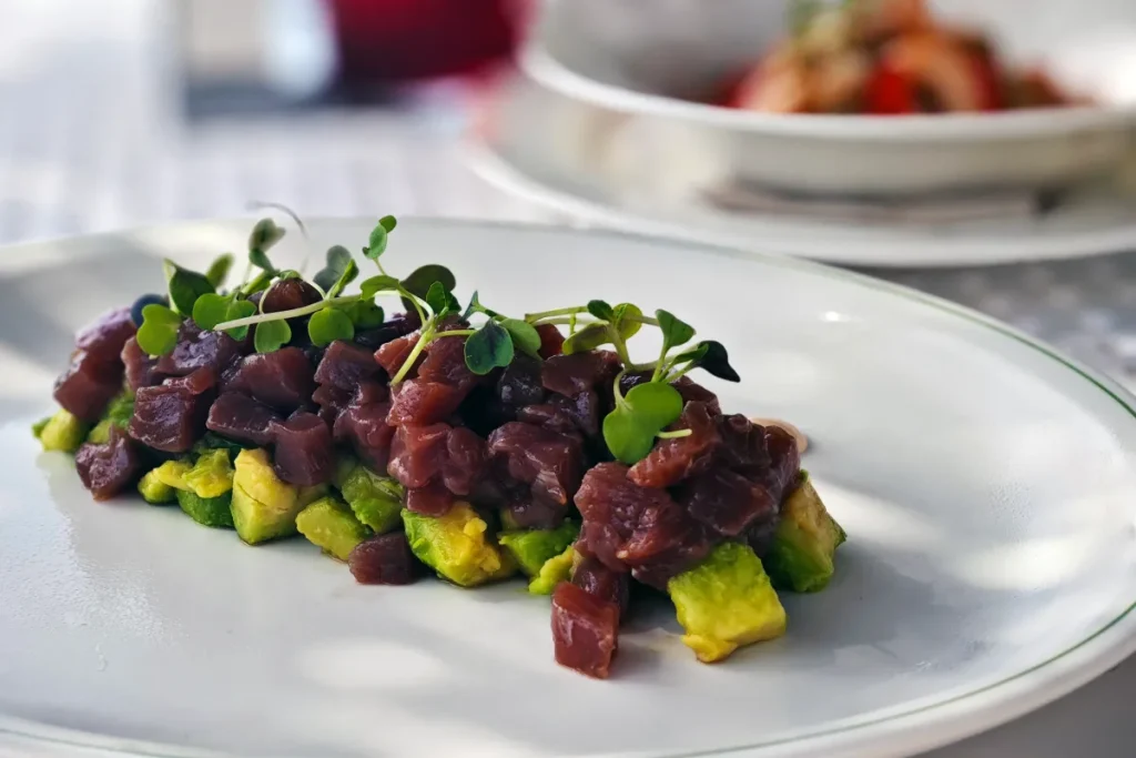 Plato con cubos de aguacate y carne oscura con brotes verdes en primer plano