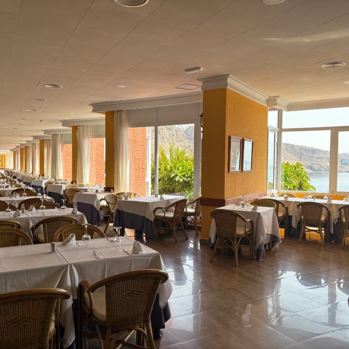 Comedor de hotel con mesas, sillas y ventanas con vista a la monta&ntilde;a.
