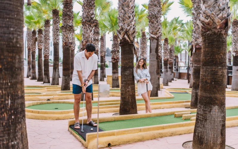 Pareja jugando golf en un campo con palmeras y hoyos de mini-golf.