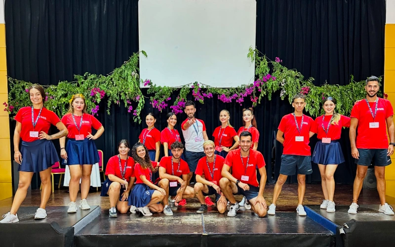 Equipo de j&oacute;venes con camisetas rojas y fondo esc&eacute;nico con flores y tel&oacute;n