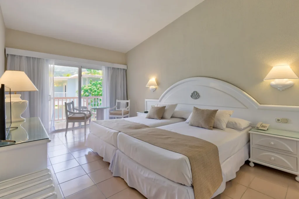 Habitaci&oacute;n de hotel con cama doble, mesita y acceso al balc&oacute;n con vistas verdes