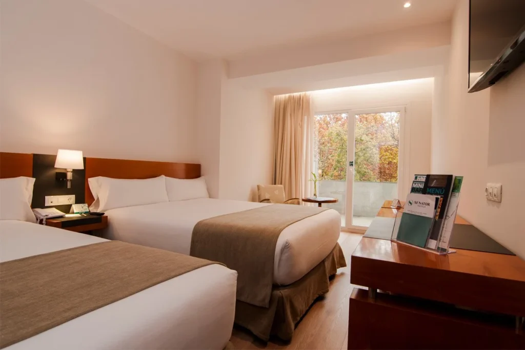 Habitaci&oacute;n de hotel moderna con dos camas, escritorio y vista al exterior