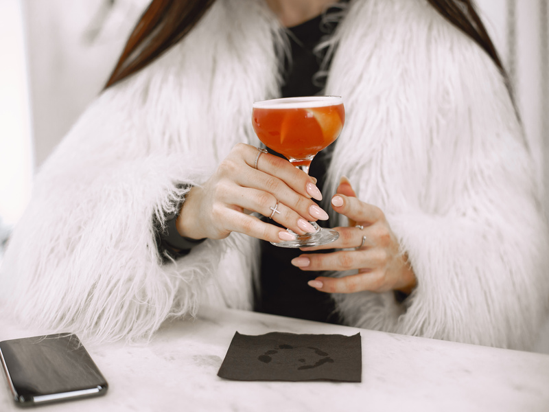 Una chica con un abrigo de pelo blanco sujetando un cocktail cosmopolitan