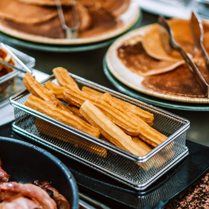 Churros en una canasta met&aacute;lica junto a platos con panqueques.